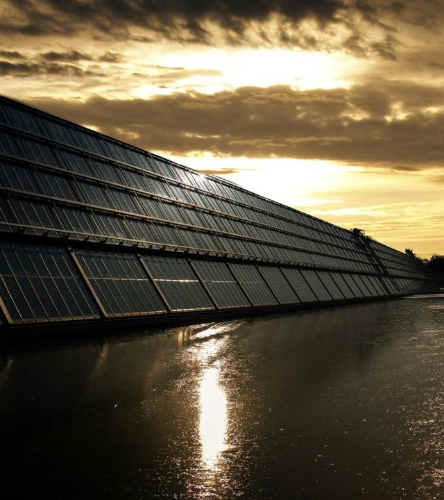 Silhouetted solar panels reflect sunset in tranquil waters, showcasing renewable energy.